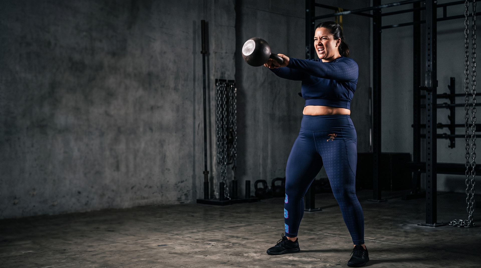 Athlete in navy Big Belly Athletics gear swinging a kettlebell in a gym